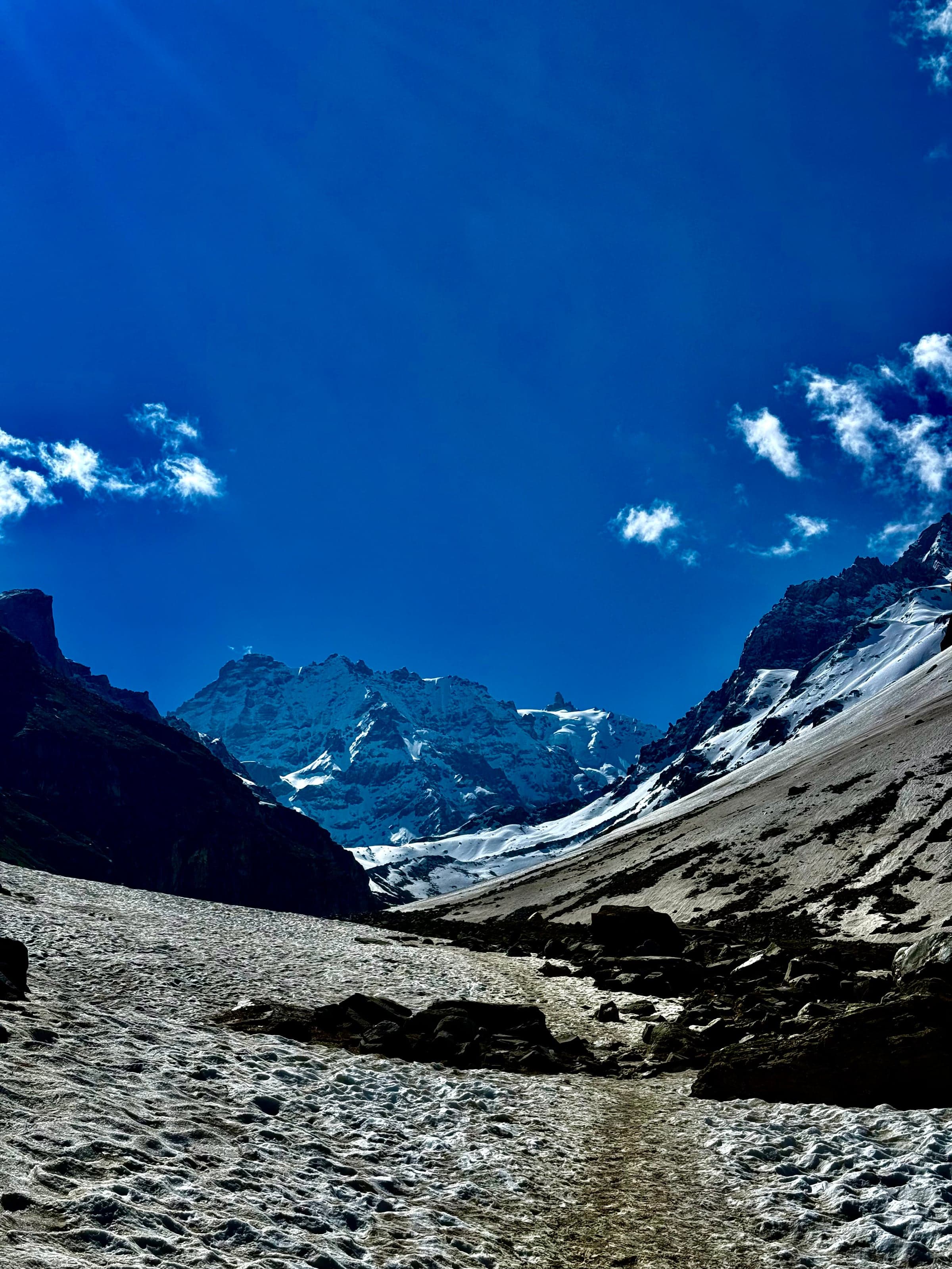 A snowfield leading up a valley to a snow-covered peak under a deep blue sky