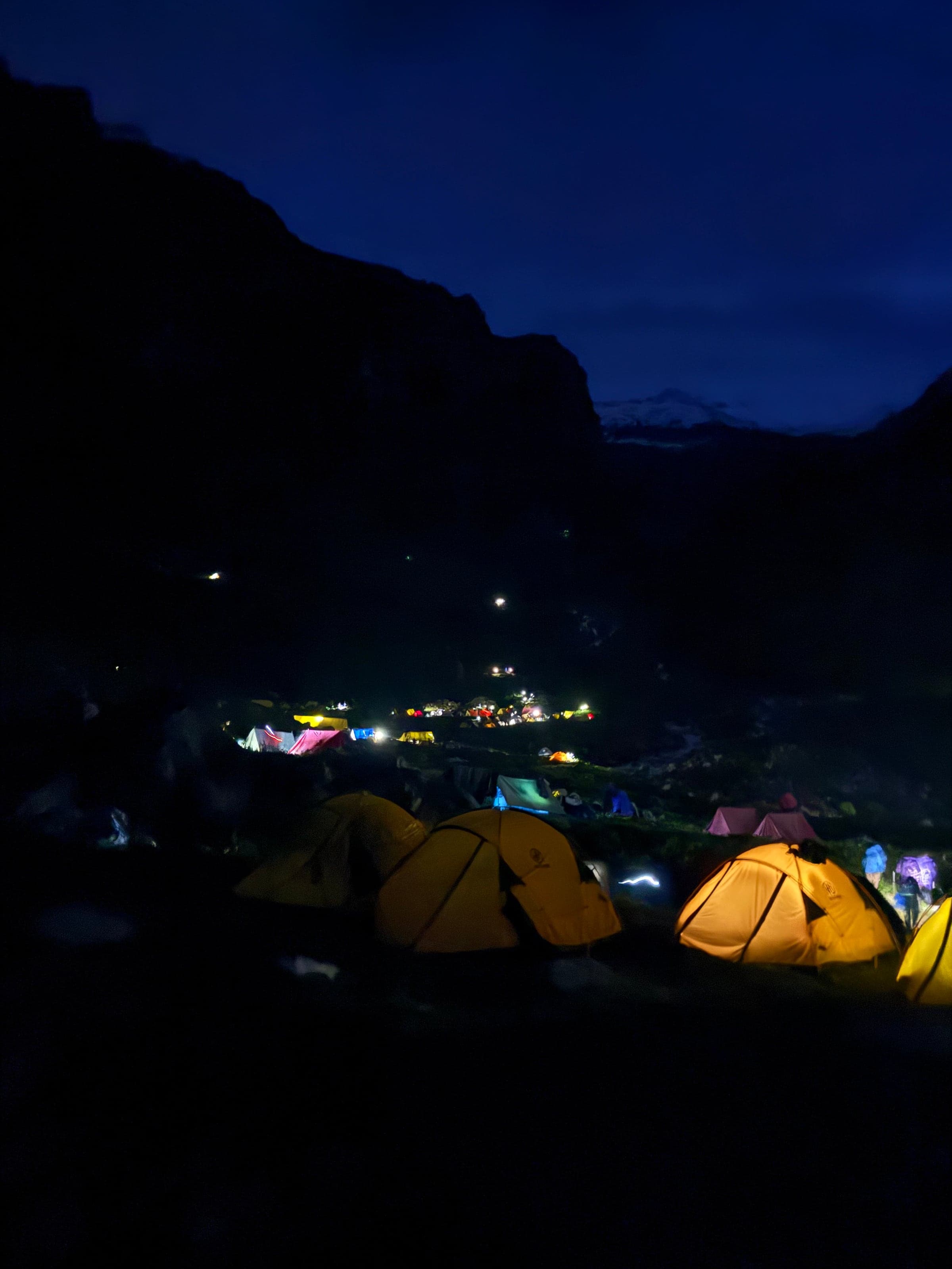 Glowing yellow tents at a mountain campsite at dusk, with more camp lights down the valley