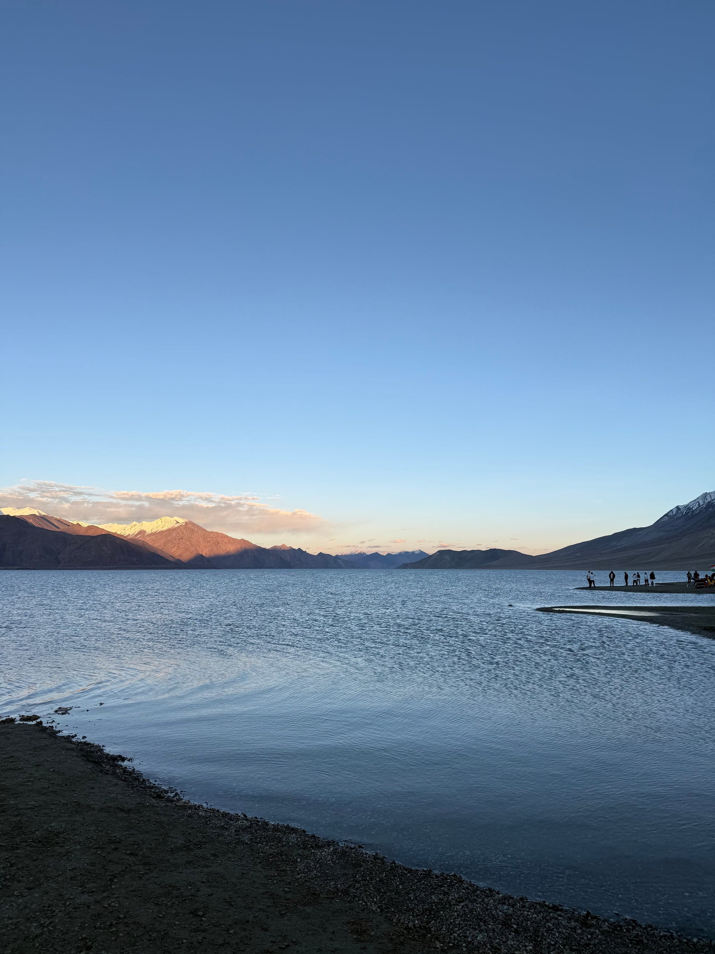 A calm lake at sunset with the last light on distant peaks and people on the far shore