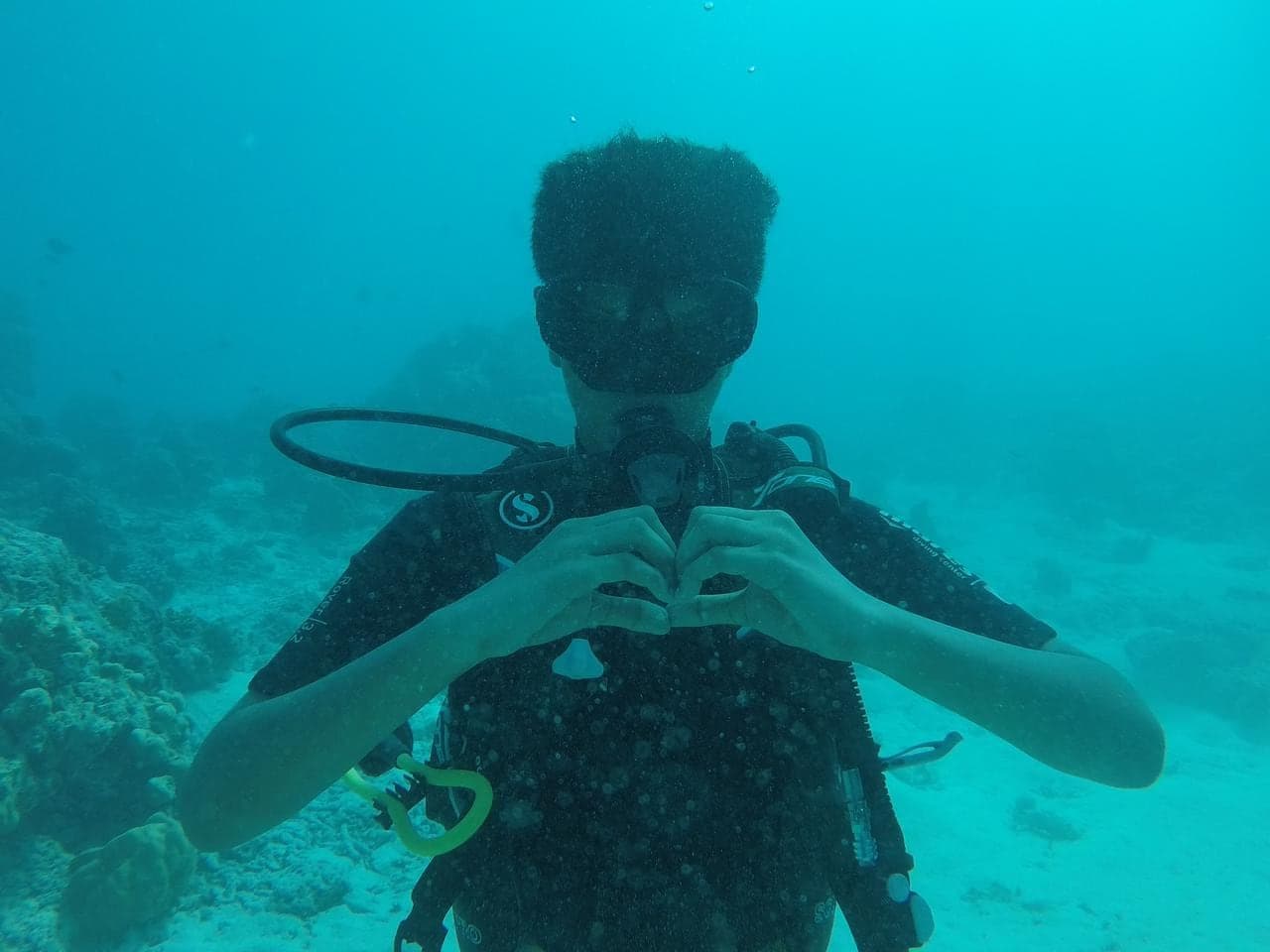 A scuba diver underwater making a heart shape with both hands